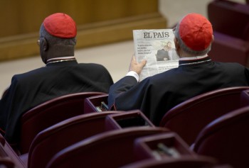 Spanish Cardinal Ricardo Blazquez Perez, right, reads a newspaper showing a picture of gay bishop Krzysztof Charamsa and his partner Eduard before the start of the morning session of the Synod of bishops on family issues, at the Vatican, Friday, Oct. 9, 2015. Last week the Vatican fired Charamsa who came out as gay on the eve of the meeting of the world's bishops. (AP Photo/Alessandra Tarantino)